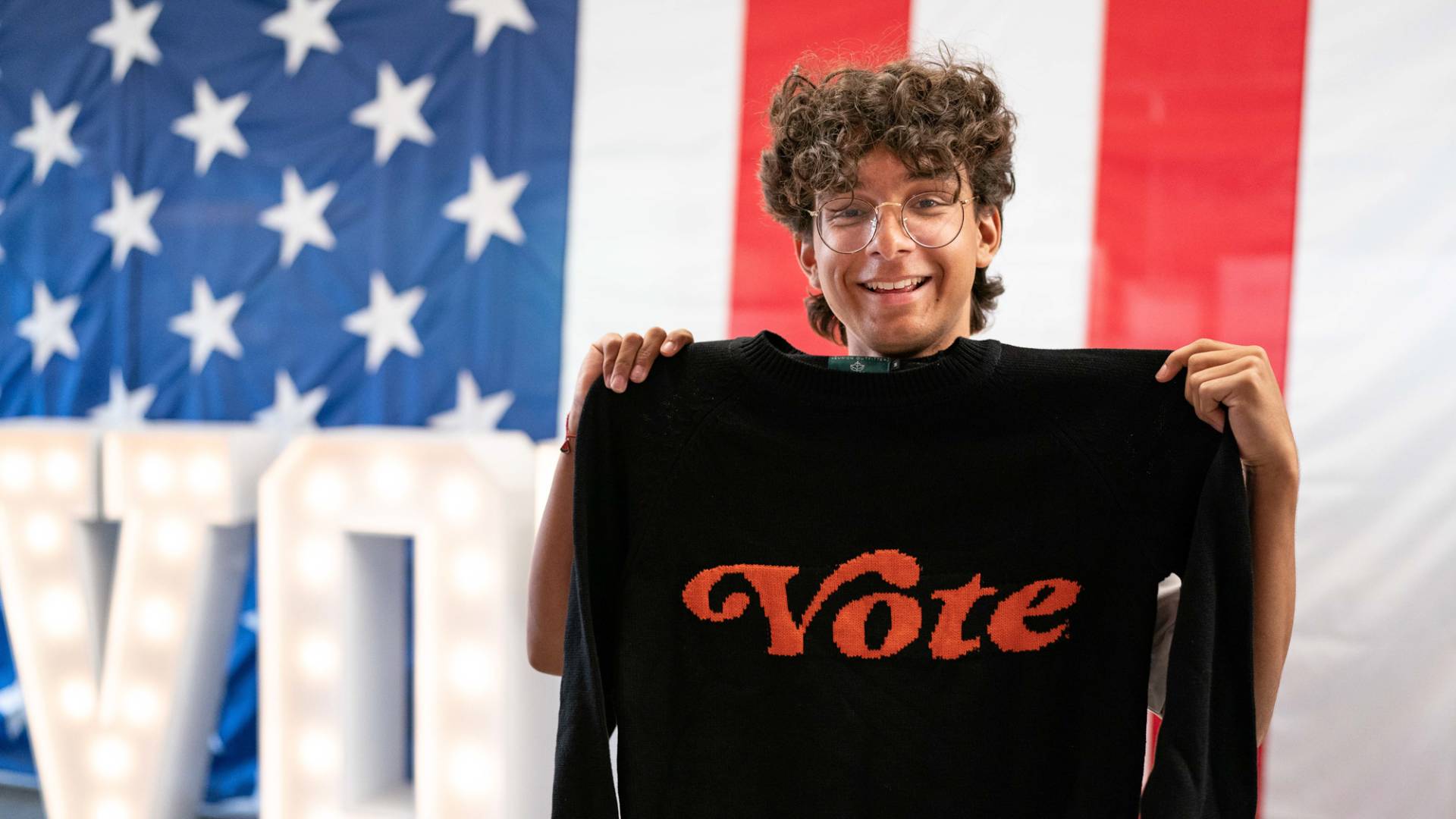 A student holding a black sweater with "Vote" written in orange in front.