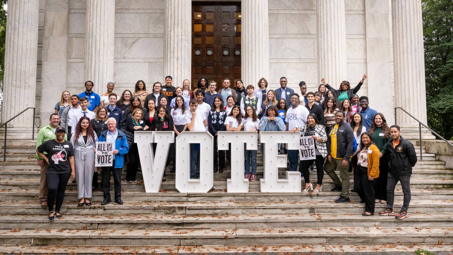 Large group of people on a staircase posing for the photo, a large "vote" sign in the middle.