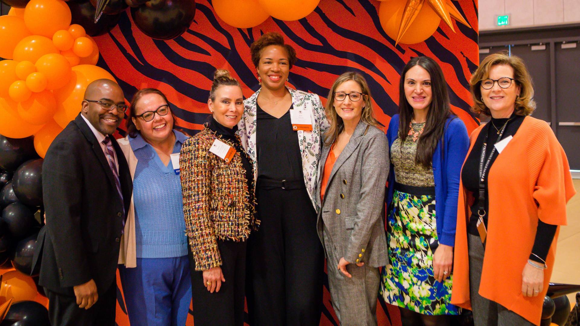 Staff pose in front of orange and black banner