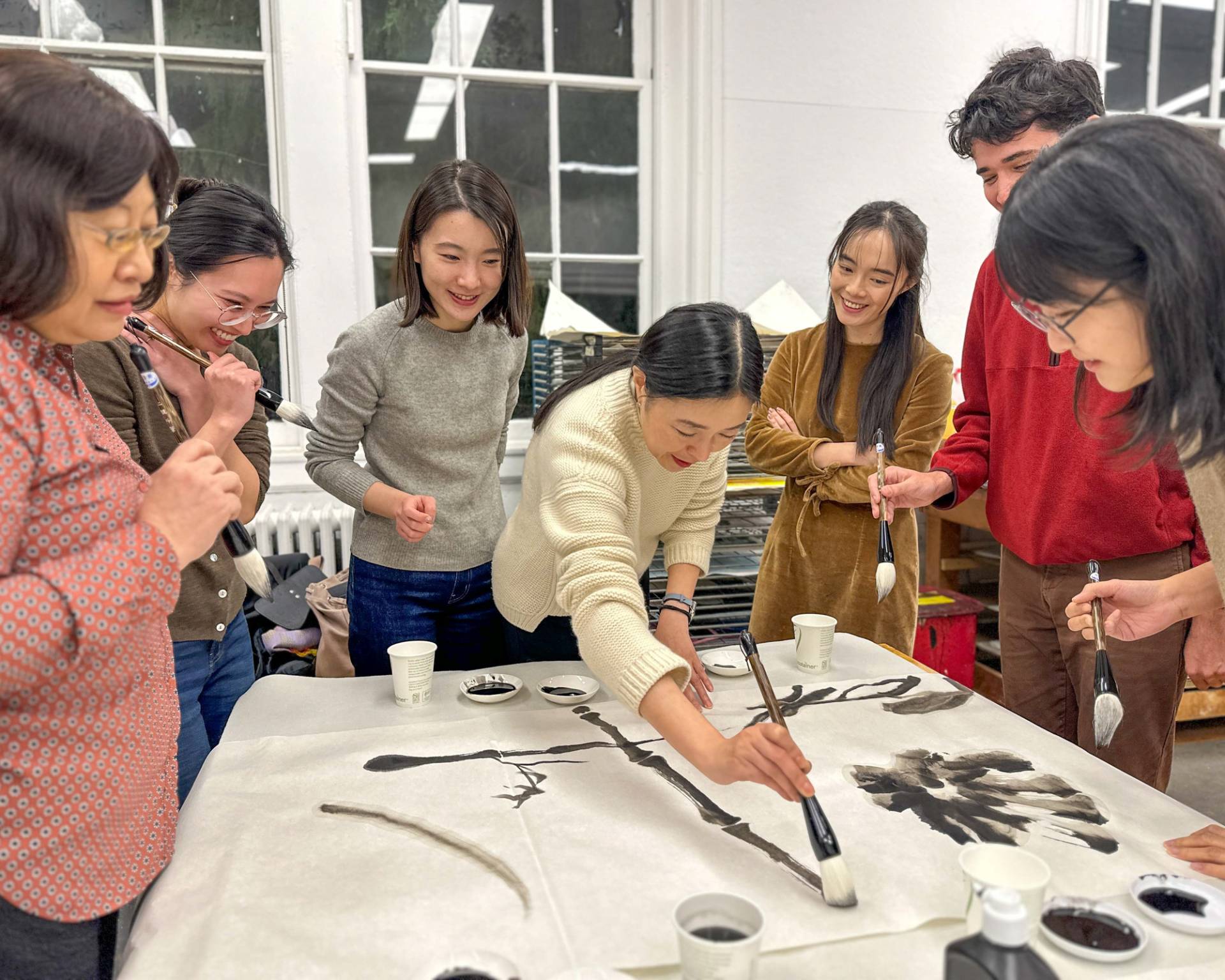 A professor skillfully writes with a Chinese brush and black ink on a large surface of paper.
